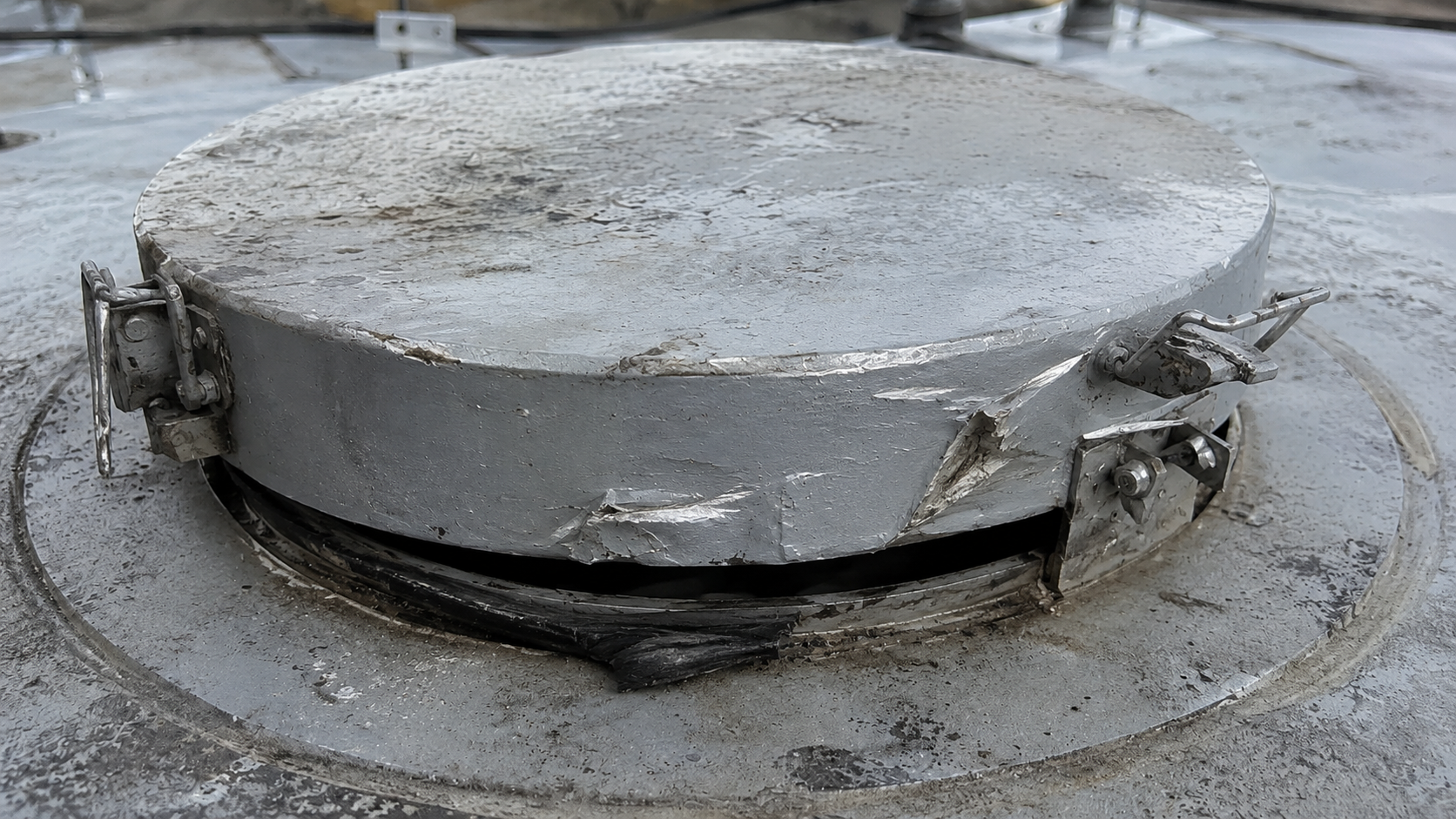 Water tank hatch showing pry marks and damaged latch hardware after vandalism
